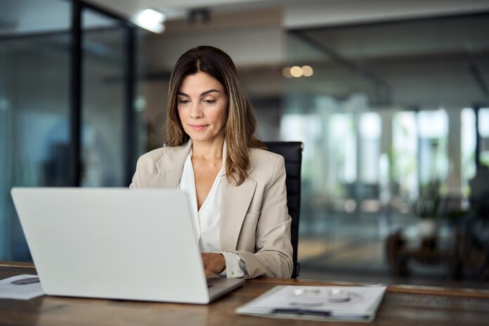 Busy mature professional business woman looking at laptop working in office.